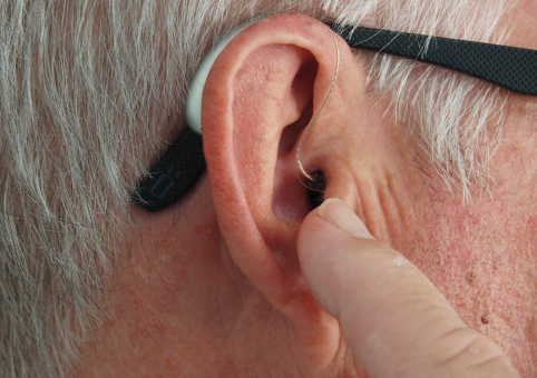 A man pointing to his ear. He is wearing a hearing aid