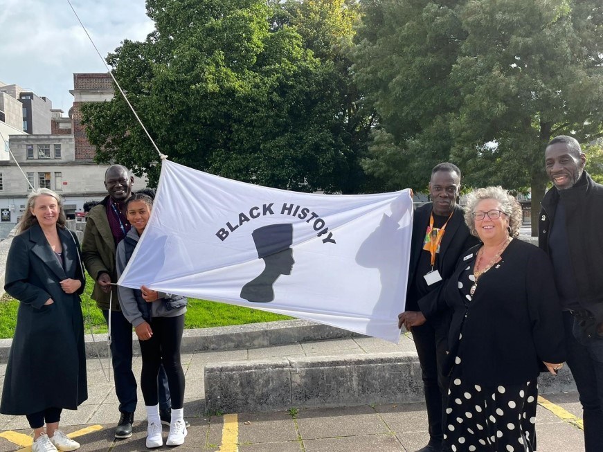 A group of people including the Right Worshipful Lord Mayor of Southampton, Councillor Jacqui Rayment displaying the Black History Month flag