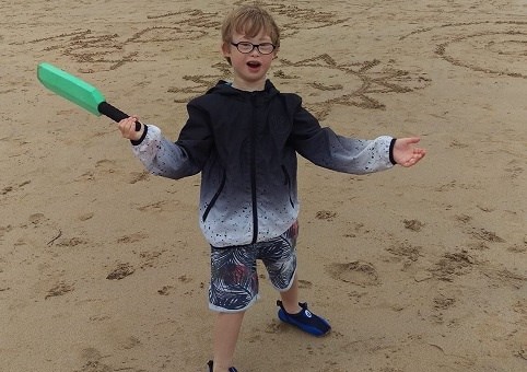 A child on a beach with a mini-cricket bat in one hand