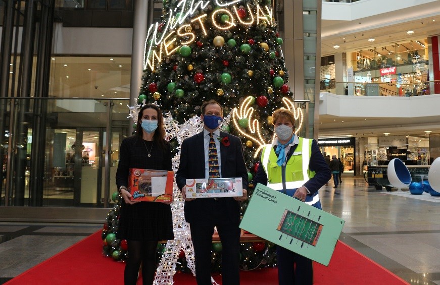 Three people, holding toys, standing in front of a Christmas tree in Westquay shopping centre