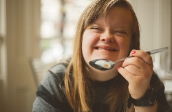 A woman smiling. She is holding a spoon with food on it