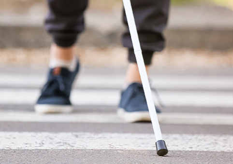 Close up of mobility cane and feet on a zebra crossing