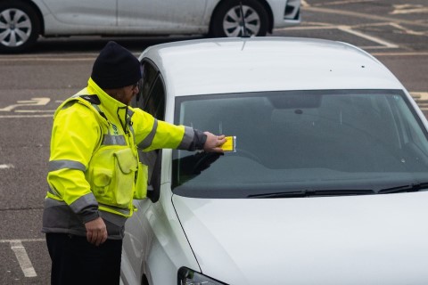 A parking warden putting a Penalty Charge Notice on a car windscreen