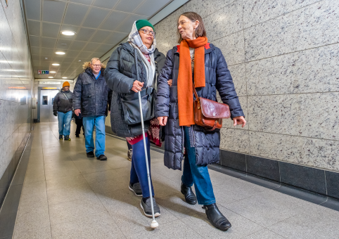 A lady with a mobility stick being guided on the Underground