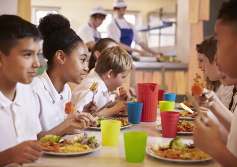 Students sitting at a table eating together with the chefs in the background