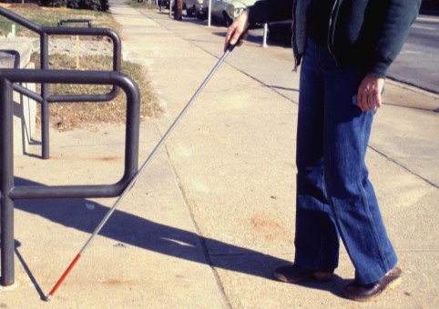 A man using a red and white deafblind cane outside