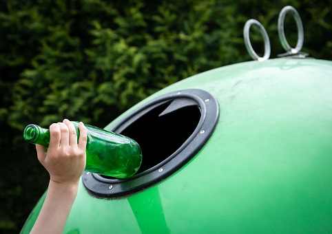 A green bottle being placed into a recycling bank