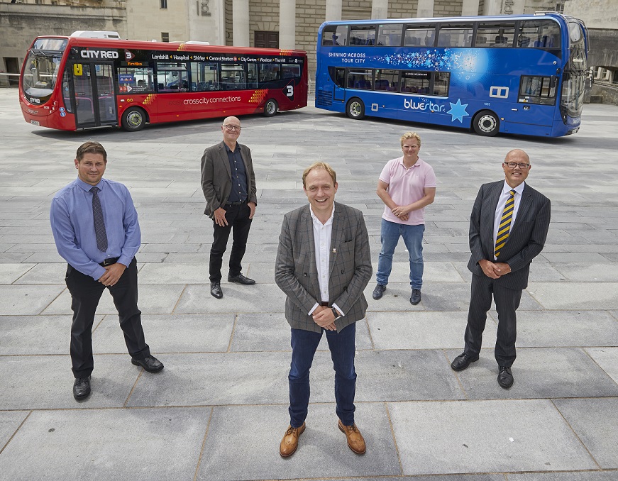 Several people standing in front of two buses at the guildhall