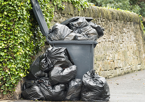 An overflowing bin on the street with more rubbish piled around it