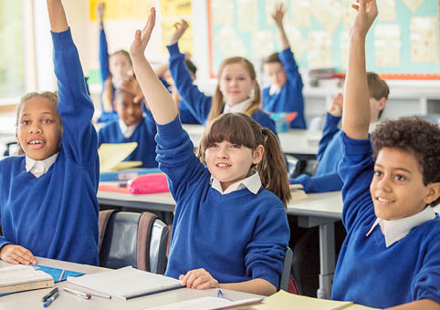 Children putting their hands up in class