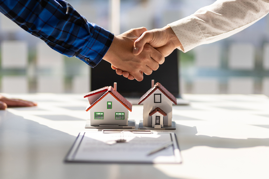 Two people shaking hands over some paperwork and two models of houses Two people shaking hands over some paperwork and two models of houses