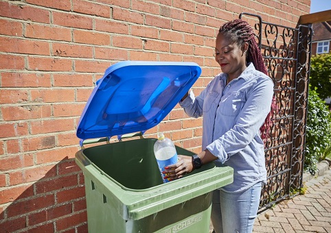 A woman putting a plastic bottle in her blue lidded recycling bin