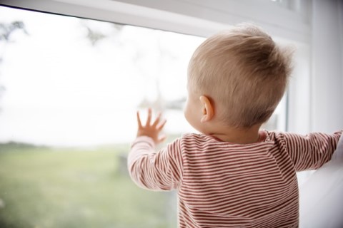 A child looking out a window and pressing their hand against it