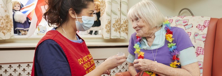 Carer giving medication to an elderly woman