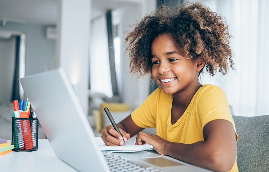 Girl writing notes while looking at a laptop computer