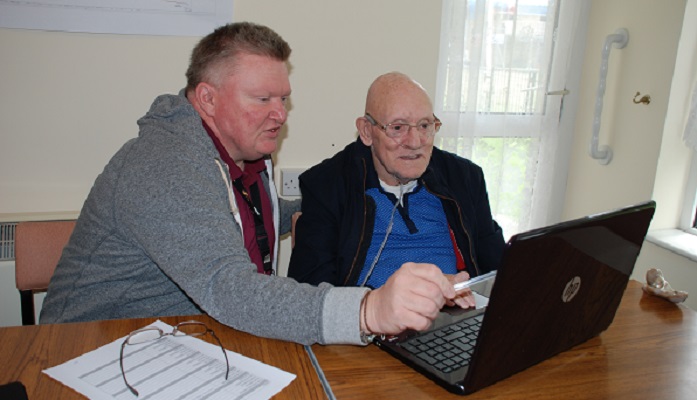 Elderly man being helped to use a laptop