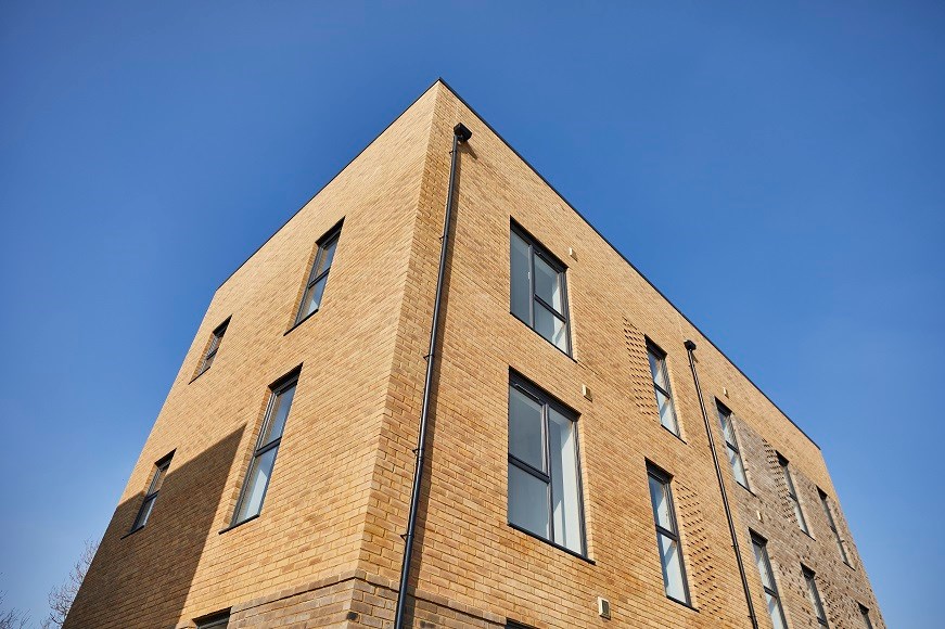 Image of brown brick building with windows with black panels on a sunny day with a blue sky above the building