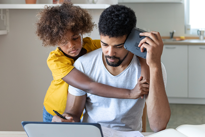 A man looking concerned about paperwork while being hugged by a child A man looking concerned about paperwork while being hugged by a child