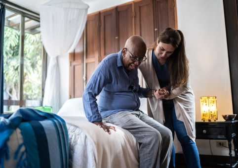 Elderly man being helped off bed by carer