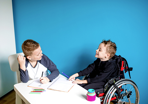 Two boys writing and chatting. One of them is sitting in a wheelchair