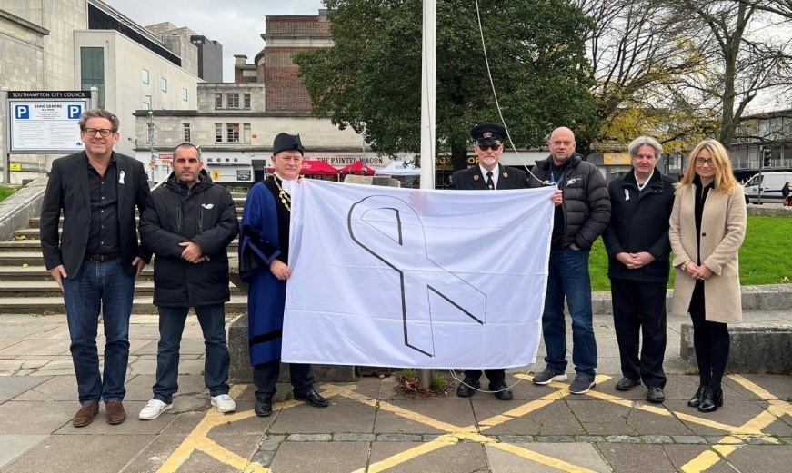 Several people holding a flag with a white ribbon on it