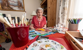 Elderly woman at table with paint brushes