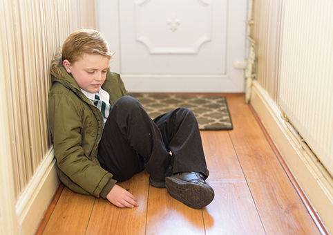 A child sitting on the floor, by their front door, at home