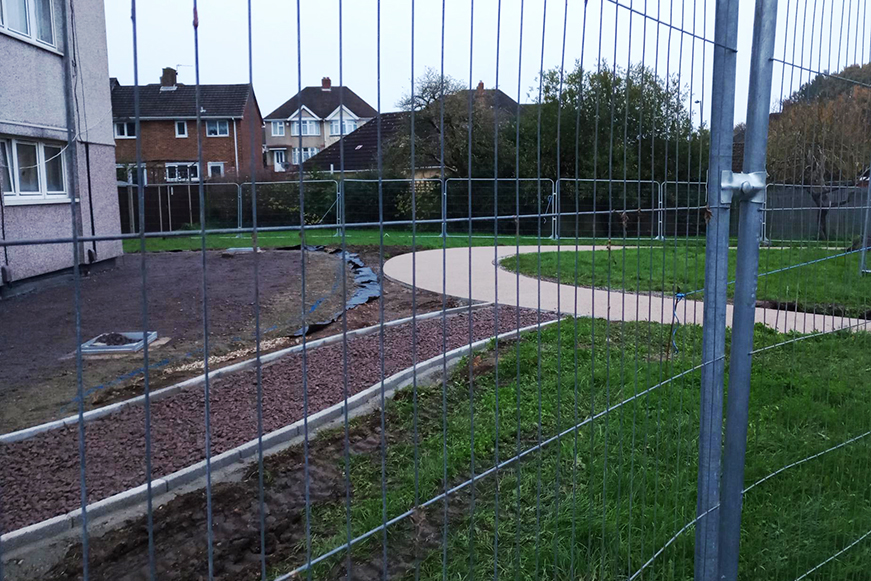 Landscaping improvements including a new path and underground plastic sheeting, surrounded by a temporary fence.