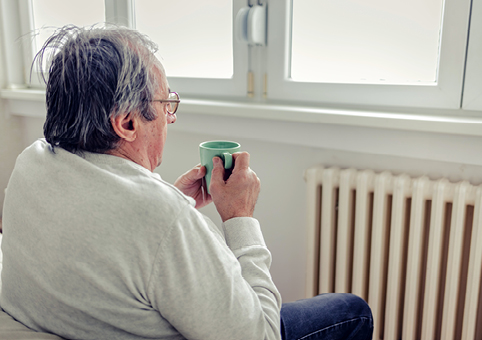 An elderly man sitting by the radiator