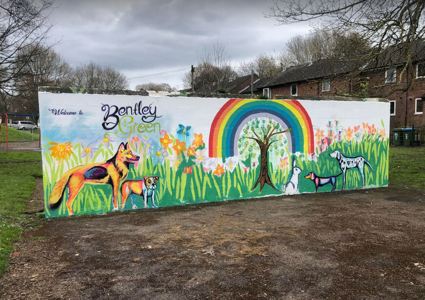 A painted mural showing flowers, a tree, a rainbow, several dogs and a hare. It says "Welcome to Bentley Green"