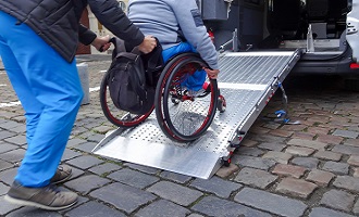 Some in wheelchair being pushed up vehicle ramp