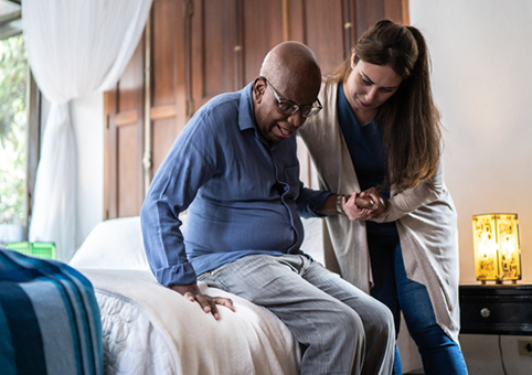 Woman helping elderly man out of bed