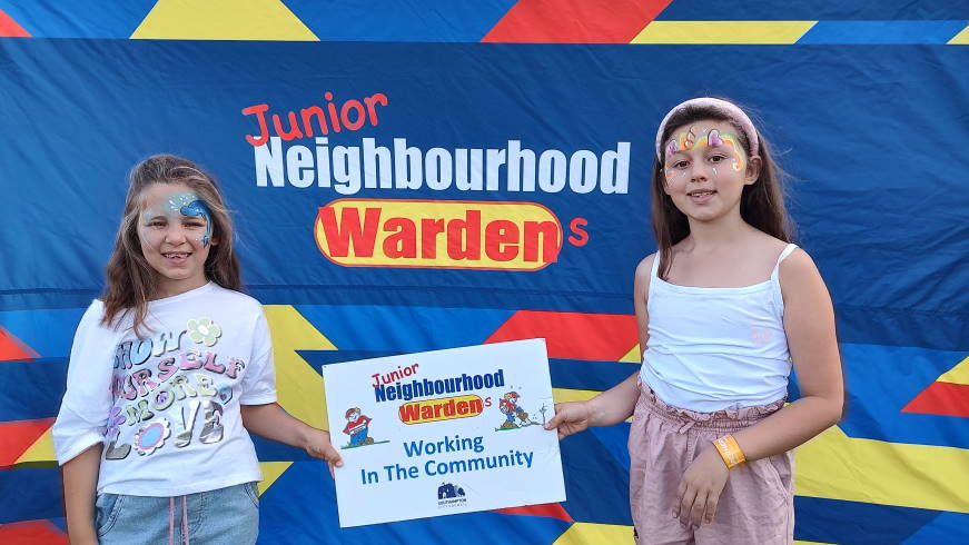 Two girls in front of a Junior Wardens banner