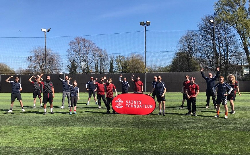 Graduates stand on a training field with a Saints Foundation sign
