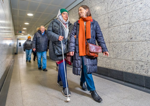 A blind woman being helped along an underpass